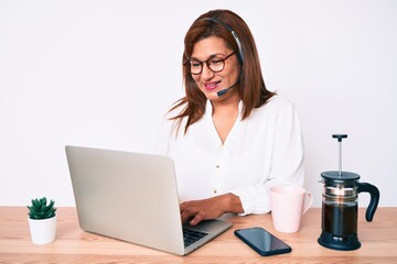 Middle age brunette hispanic woman working at the office wearing operator headset looking positive and happy standing and smiling with a confident smile showing teeth