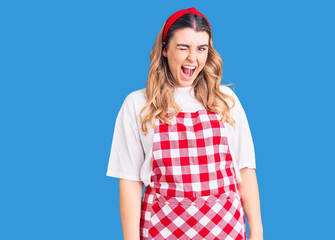 Young caucasian woman wearing apron winking looking at the camera with sexy expression, cheerful...