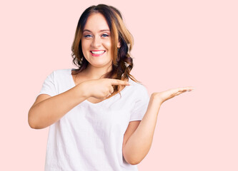 Young beautiful caucasian woman wearing casual white tshirt amazed and smiling to the camera while presenting with hand and pointing with finger.