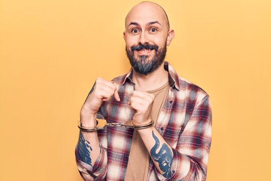 Young handsome man wearing prisoner handcuffs smiling happy pointing with hand and finger