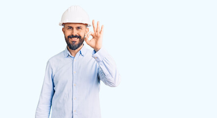Young handsome man wearing architect hardhat smiling positive doing ok sign with hand and fingers. successful expression.