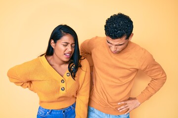 Beautiful latin young couple wearing casual clothes together suffering of backache, touching back with hand, muscular pain