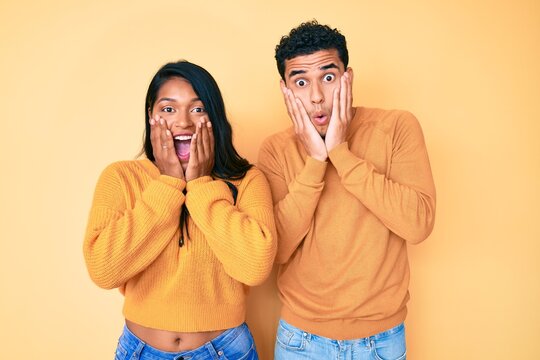 Beautiful latin young couple wearing casual clothes together afraid and shocked, surprise and amazed expression with hands on face