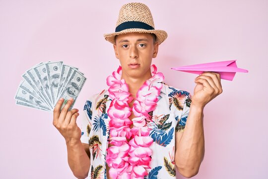 Young hispanic boy wearing summer style holding dollars and paper airplane relaxed with serious expression on face. simple and natural looking at the camera.