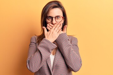 Young beautiful woman wearing business clothes and glasses shocked covering mouth with hands for mistake. secret concept.