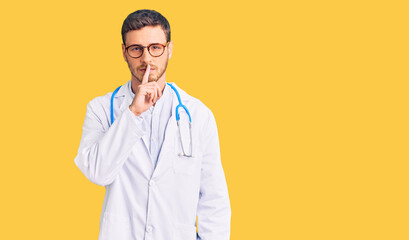 Handsome young man with bear wearing doctor uniform asking to be quiet with finger on lips. silence and secret concept.