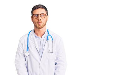 Handsome young man with bear wearing doctor uniform making fish face with lips, crazy and comical gesture. funny expression.