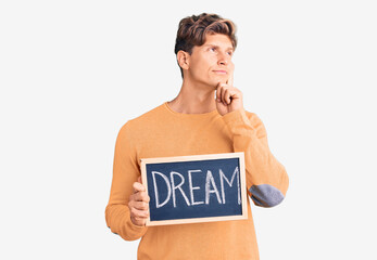 Young handsome man holding blackboard with dream word serious face thinking about question with...