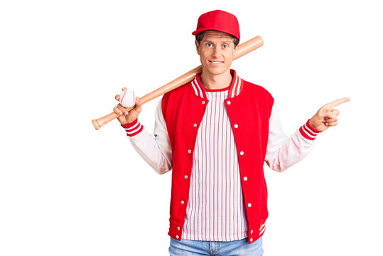 Young handsome man playing baseball holding bat and ball smiling happy pointing with hand and finger to the side
