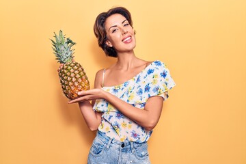 Young beautiful woman holding pineapple looking positive and happy standing and smiling with a confident smile showing teeth