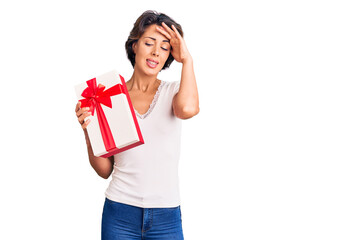 Young beautiful woman holding gift stressed and frustrated with hand on head, surprised and angry face