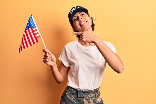 Young beautiful woman wearing usa cap holding united states flag smiling happy pointing with hand and finger