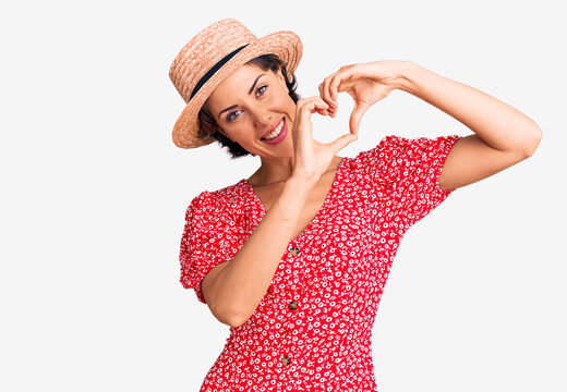 Young beautiful woman wearing summer hat smiling in love doing heart symbol shape with hands. romantic concept.