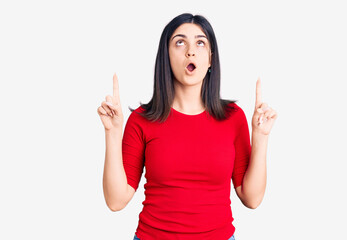 Young beautiful girl wearing casual t shirt amazed and surprised looking up and pointing with fingers and raised arms.