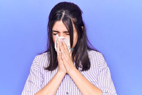 Young hispanic woman illness using paper handkerchief on nose. Standing over isoltated purple background