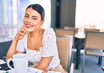 Young beautiful brunette woman smiling happy and confident. Sitting with smile on face at restaurant
