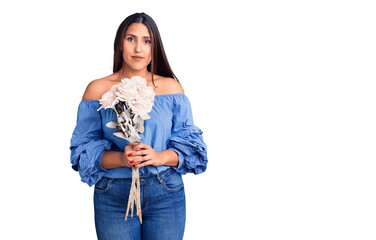 Young beautiful brunette woman holding bouquet thinking attitude and sober expression looking self...