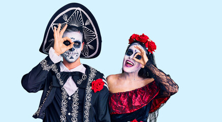 Young couple wearing mexican day of the dead costume over background doing ok gesture with hand smiling, eye looking through fingers with happy face.