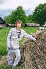 Naklejka na ściany i meble village young man in white linen clothes stands near a stack of dry hay