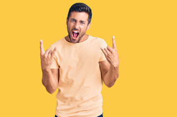 Young hispanic man wearing casual clothes shouting with crazy expression doing rock symbol with hands up. music star. heavy concept.