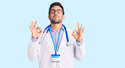 Young hispanic man wearing doctor uniform and stethoscope relaxed and smiling with eyes closed doing meditation gesture with fingers. yoga concept.