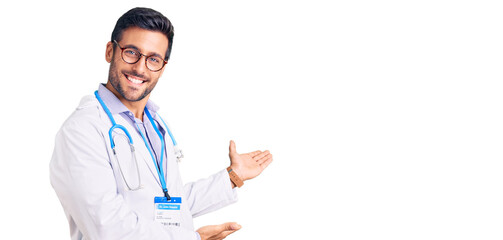 Young hispanic man wearing doctor uniform and stethoscope inviting to enter smiling natural with...