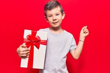 Cute blond kid holding gift smiling happy pointing with hand and finger to the side