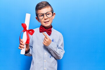 Cute blond kid wearing nerd bow tie and glasses holding diploma smiling happy pointing with hand...