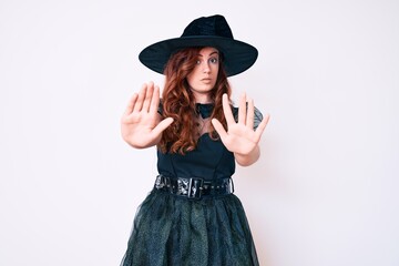 Young beautiful woman wearing witch halloween costume doing stop gesture with hands palms, angry and frustration expression