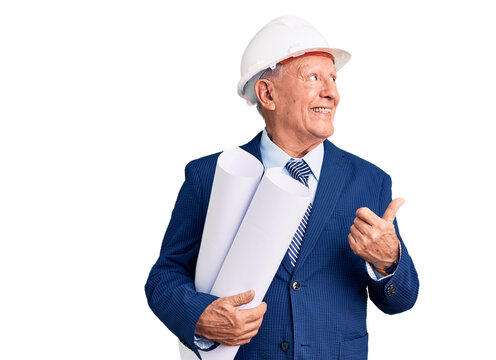 Senior handsome grey-haired man wearing architect hardhat holding blueprints pointing thumb up to the side smiling happy with open mouth