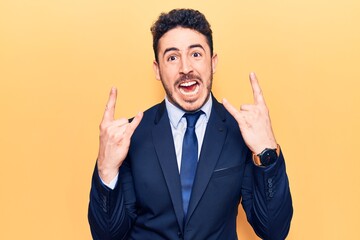 Young hispanic man wearing suit shouting with crazy expression doing rock symbol with hands up. music star. heavy concept.