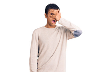 Fototapeta premium Young african amercian man wearing casual clothes peeking in shock covering face and eyes with hand, looking through fingers with embarrassed expression.