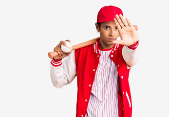 Young african amercian man playing baseball holding bat and ball with open hand doing stop sign with serious and confident expression, defense gesture