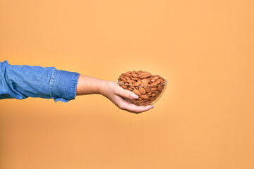 Beautiful hand of woman holding bowl with baked german pretzels over isolated yellow background