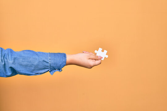 Hand of caucasian young woman holding piece of puzzle over isolated yellow background