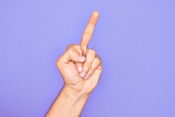 Hand of caucasian young man showing fingers over isolated purple background showing provocative and rude gesture doing fuck you symbol with middle finger