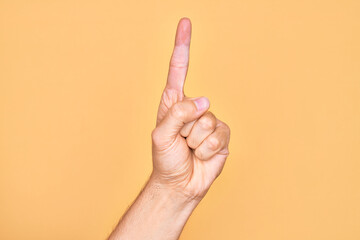 Hand of caucasian young man showing fingers over isolated yellow background counting number one using index finger, showing idea and understanding