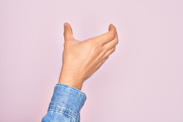Hand of caucasian young man showing fingers over isolated pink background holding invisible object, empty hand doing clipping and grabbing gesture