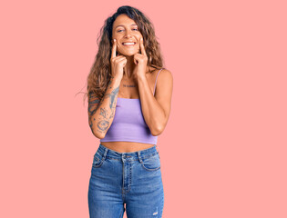 Young hispanic woman with tattoo wearing casual clothes smiling with open mouth, fingers pointing and forcing cheerful smile