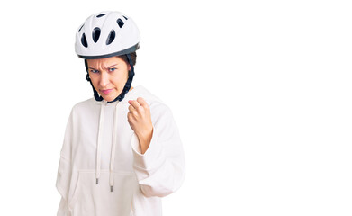 Beautiful brunette young woman wearing bike helmet and sporty clothes angry and mad raising fist frustrated and furious while shouting with anger. rage and aggressive concept.