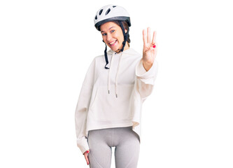 Beautiful brunette young woman wearing bike helmet and sporty clothes showing and pointing up with fingers number three while smiling confident and happy.