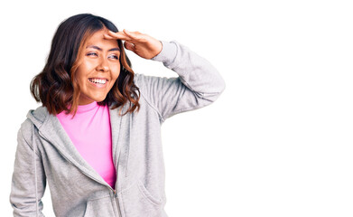 Young beautiful mixed race woman wearing casual sporty clothes very happy and smiling looking far away with hand over head. searching concept.