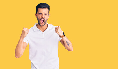 Young handsome hispanic man wearing casual clothes angry and mad raising fists frustrated and furious while shouting with anger. rage and aggressive concept.