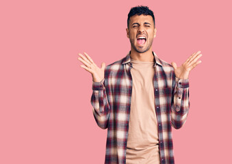 Naklejka premium Young hispanic man wearing casual clothes celebrating mad and crazy for success with arms raised and closed eyes screaming excited. winner concept