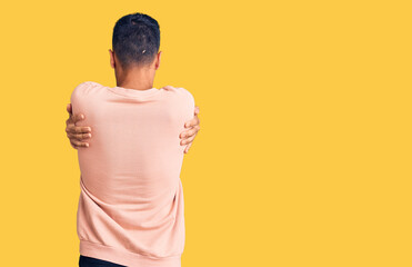 Young hispanic man wearing casual clothes hugging oneself happy and positive from backwards. self...