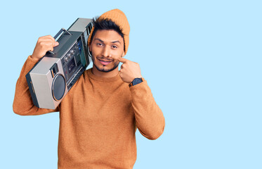 Handsome latin american young man holding boombox, listening to music pointing with hand finger to face and nose, smiling cheerful. beauty concept