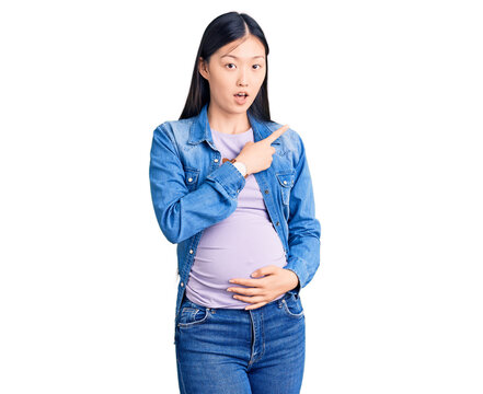 Young beautiful chinese woman pregnant expecting baby surprised pointing with finger to the side, open mouth amazed expression.