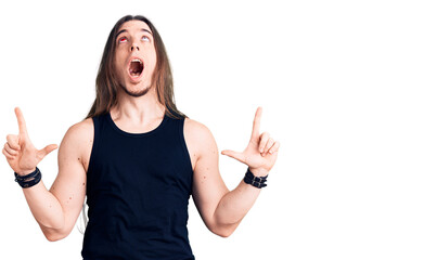 Young adult man with long hair wearing rocker style with black clothes and contact lenses amazed...