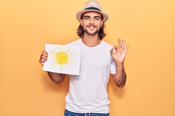 Young handsome man holding sun draw doing ok sign with fingers, smiling friendly gesturing excellent symbol