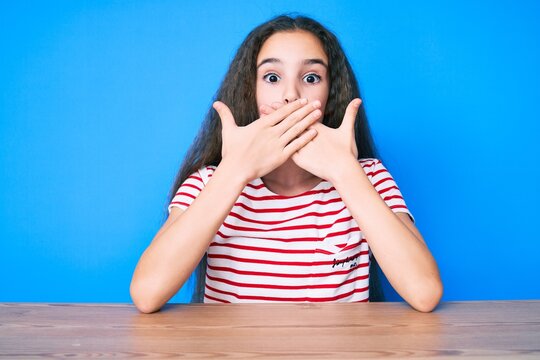 Cute hispanic child girl wearing casual clothes sitting on the table shocked covering mouth with hands for mistake. secret concept.